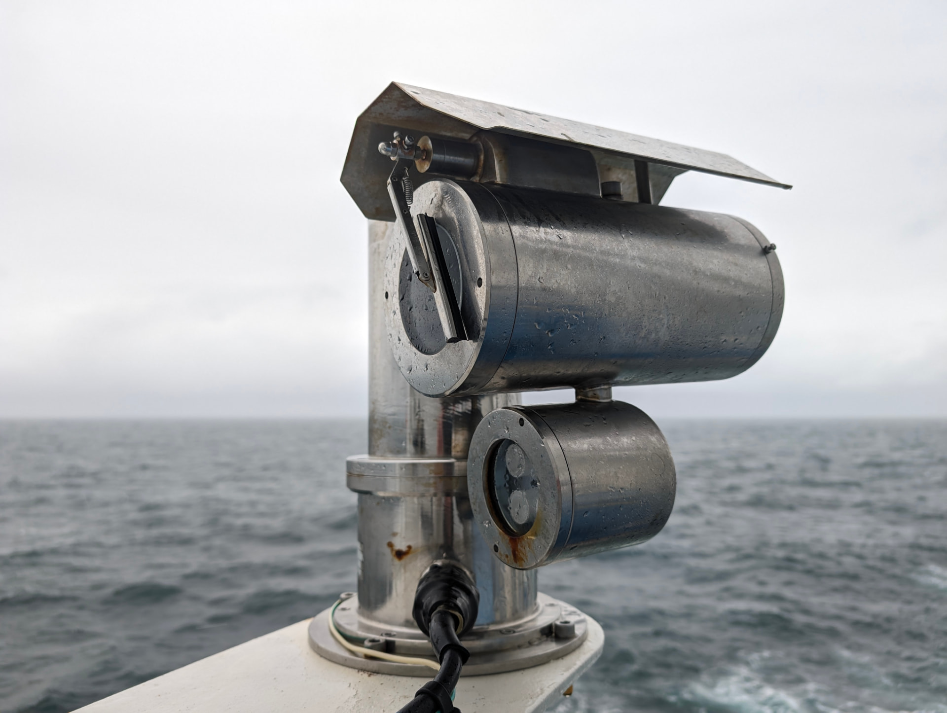 A weatherproof marine monitoring camera mounted on a vessel, looking out over open sea.