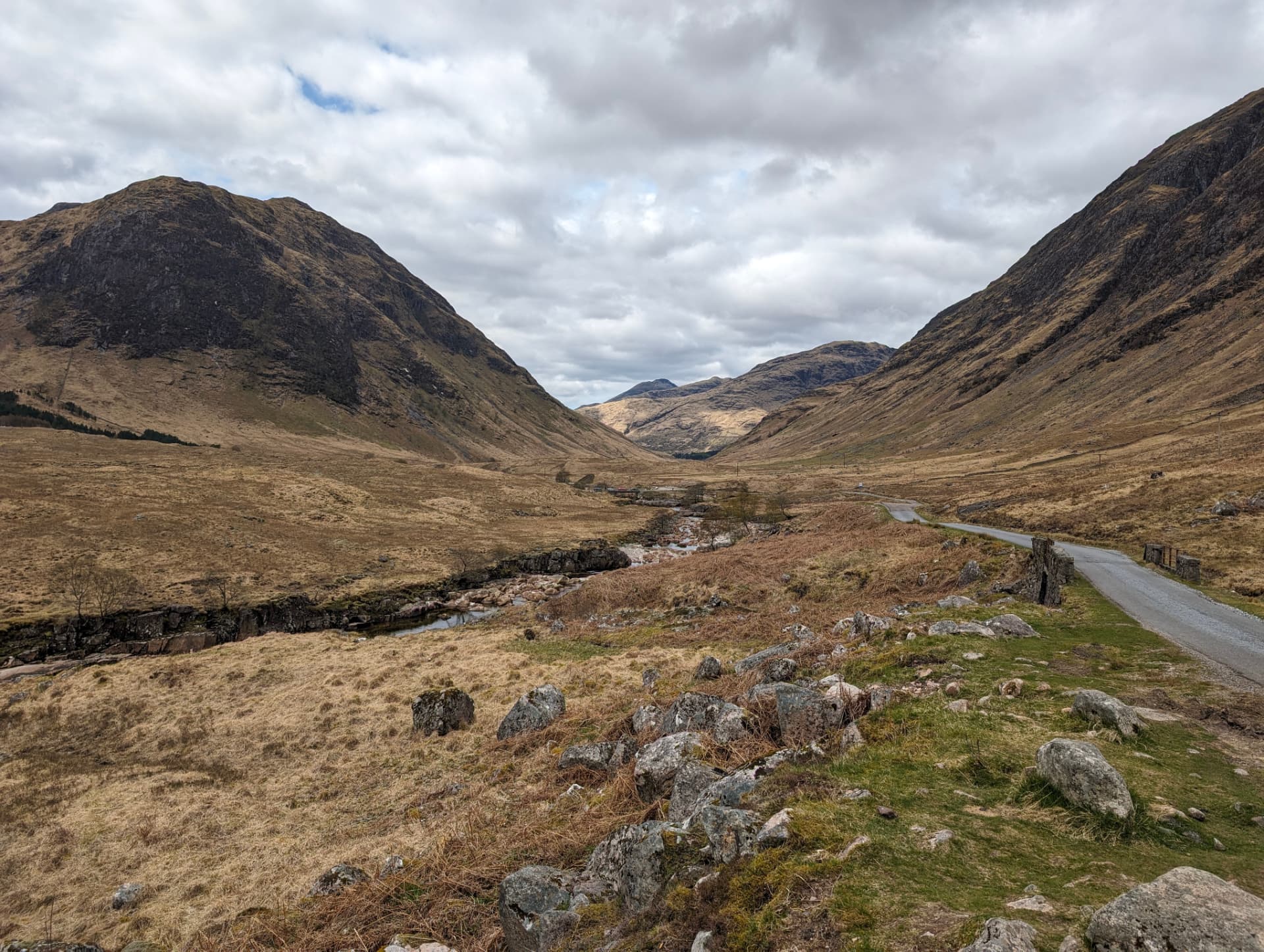 A single track road running through a remote highland glen under heavy cloud.
